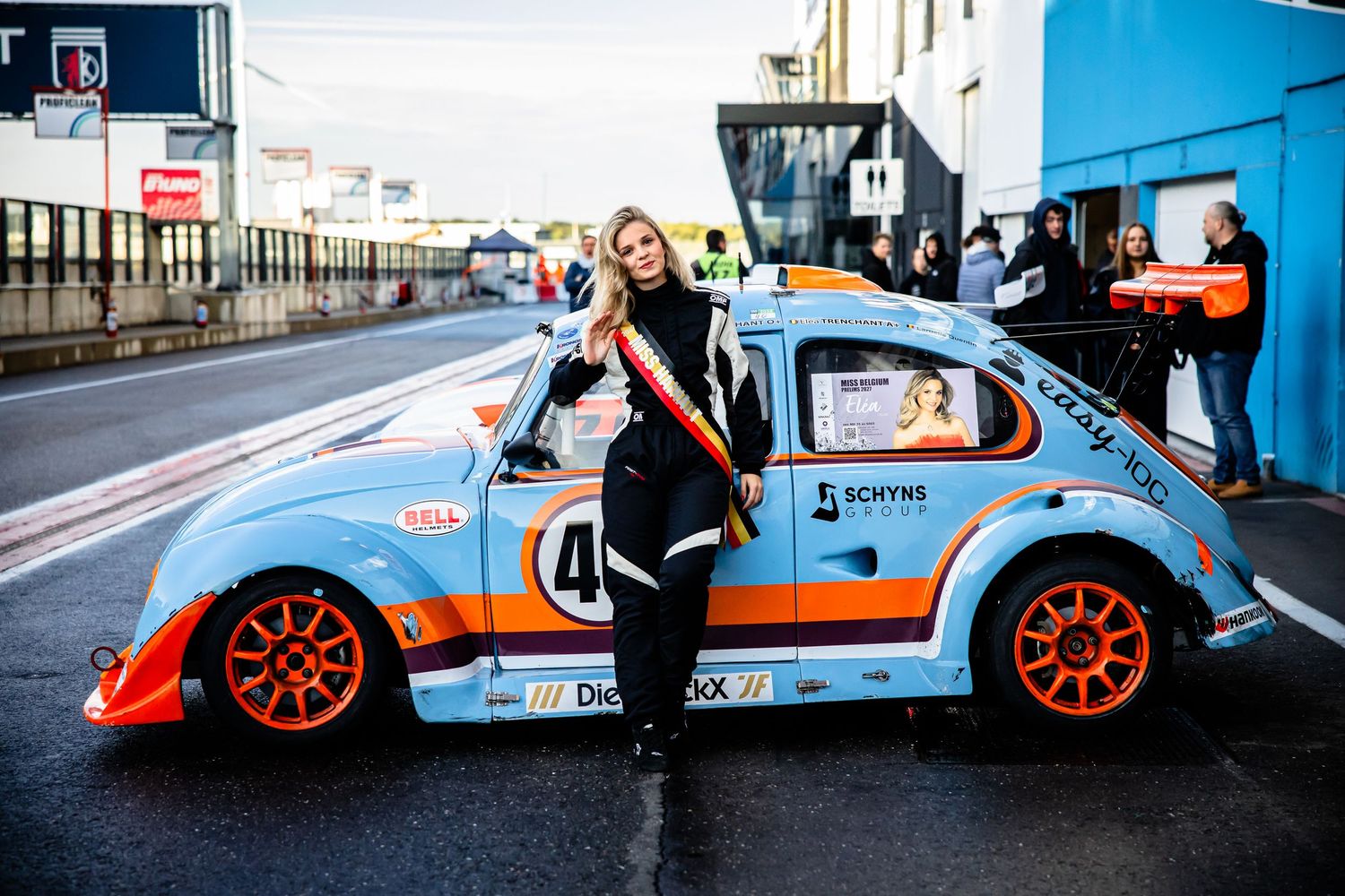 Woman posing beside a Gulf-liveried VW Beetle race car numbered 40 in a motorsport pit lane.