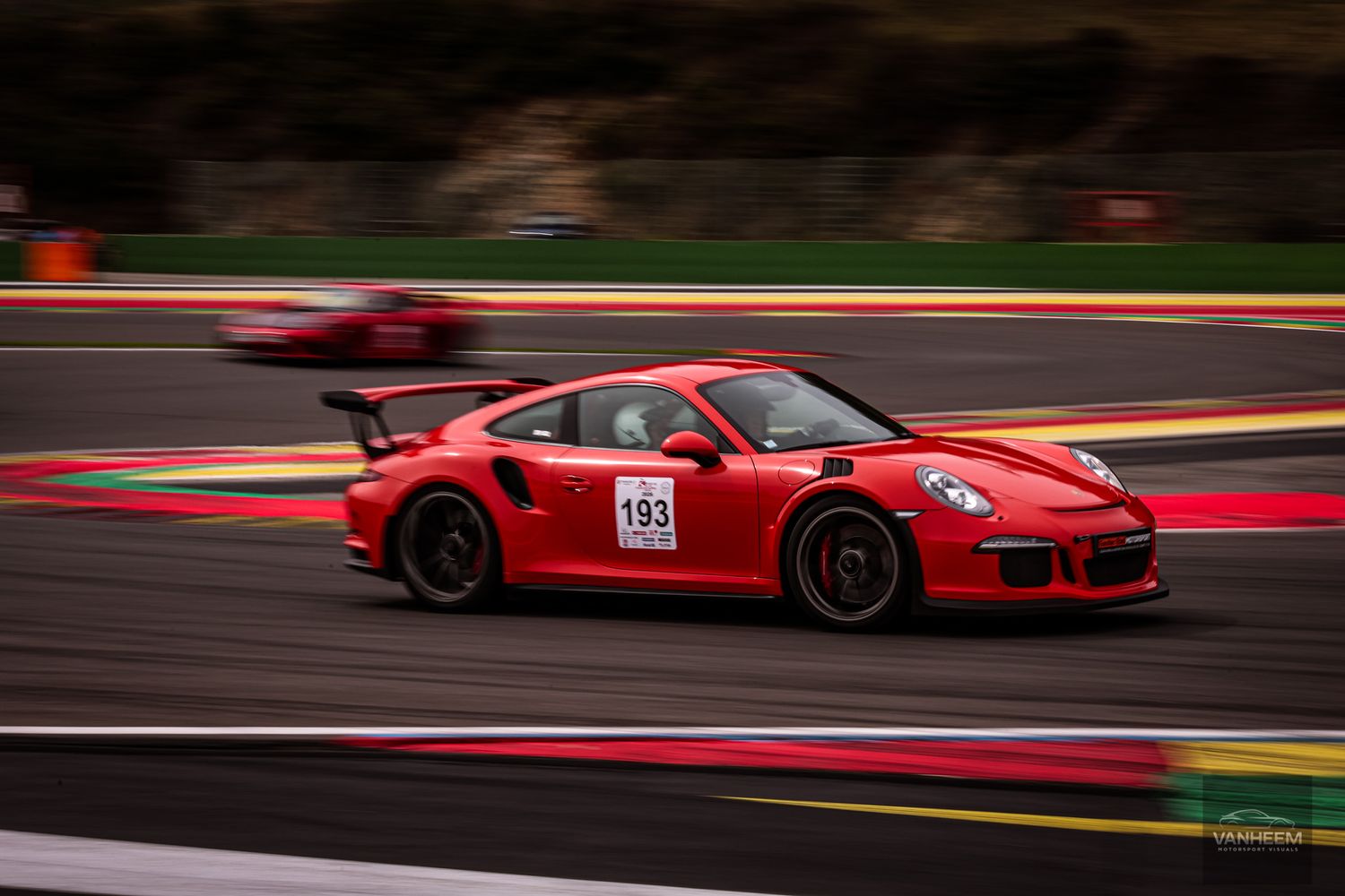 Red Porsche 911 GT3 RS race car number 193 speeding on a racing circuit track with motion blur background.