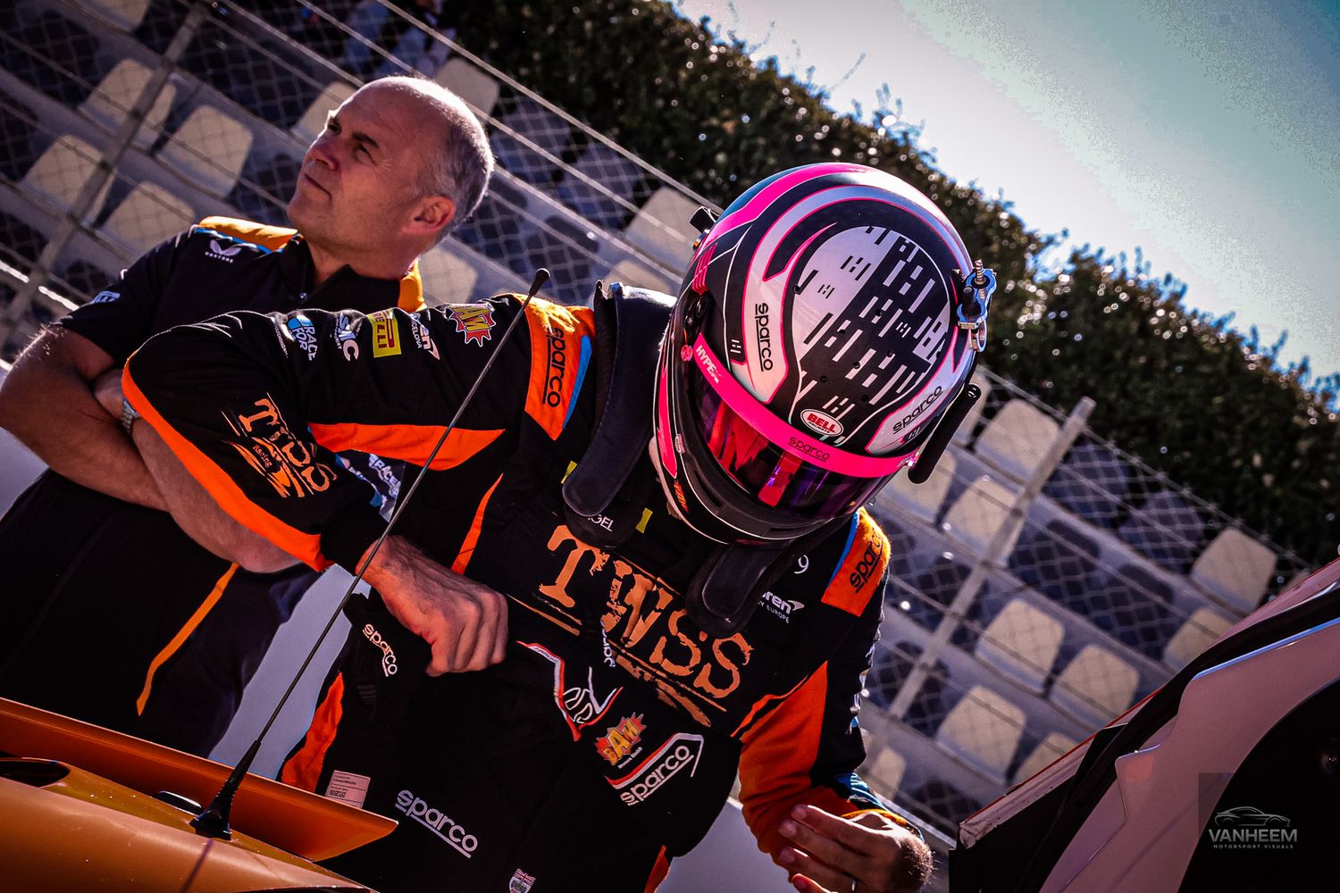 Racing team members in orange and black uniforms prepare for competition.