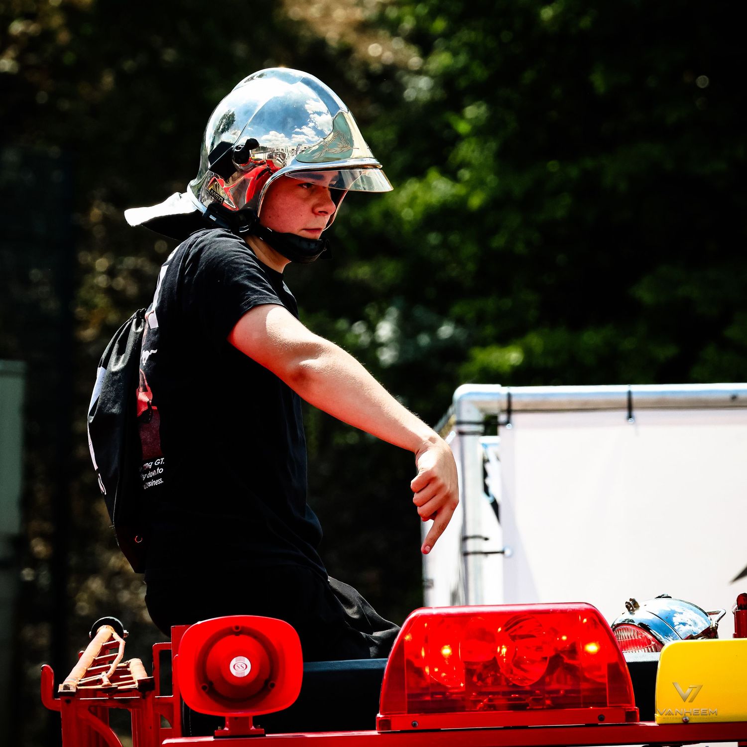 Firefighter in silver helmet and black uniform operating equipment on a red fire truck outdoors.