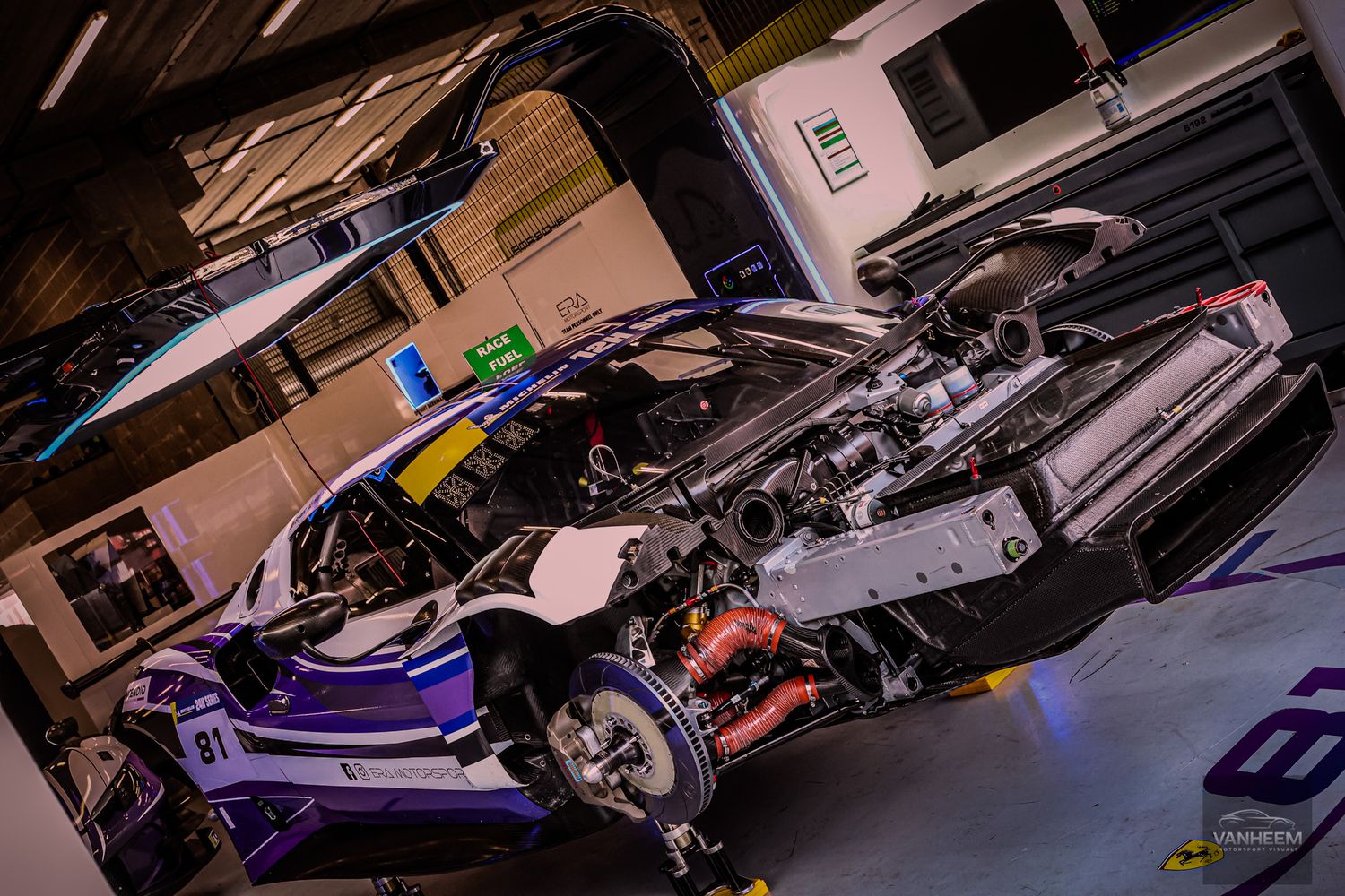 A disassembled high-performance race car with exposed engine in a professional garage workshop.