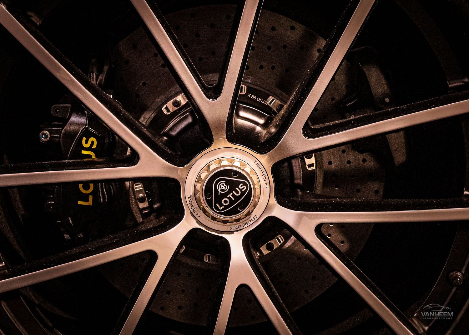 Close-up of a Lotus branded alloy wheel with yellow brake calipers and sleek spoke design on a luxury sports car.