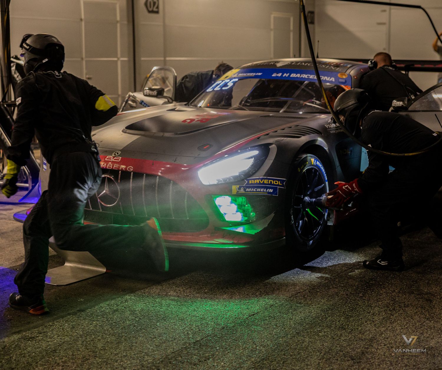 Mercedes-AMG GT3 race car in pit lane at night with crew members working under dramatic lighting.