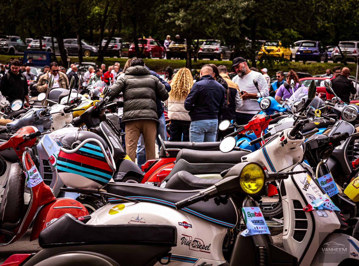 Colorful Vespa scooters parked at an outdoor rally event with people mingling in the background.