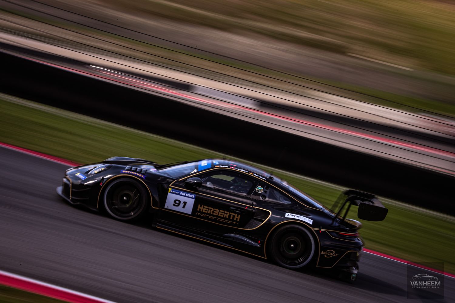 Black racing car speeds along racetrack with motion blur effect during competitive motorsport event.
