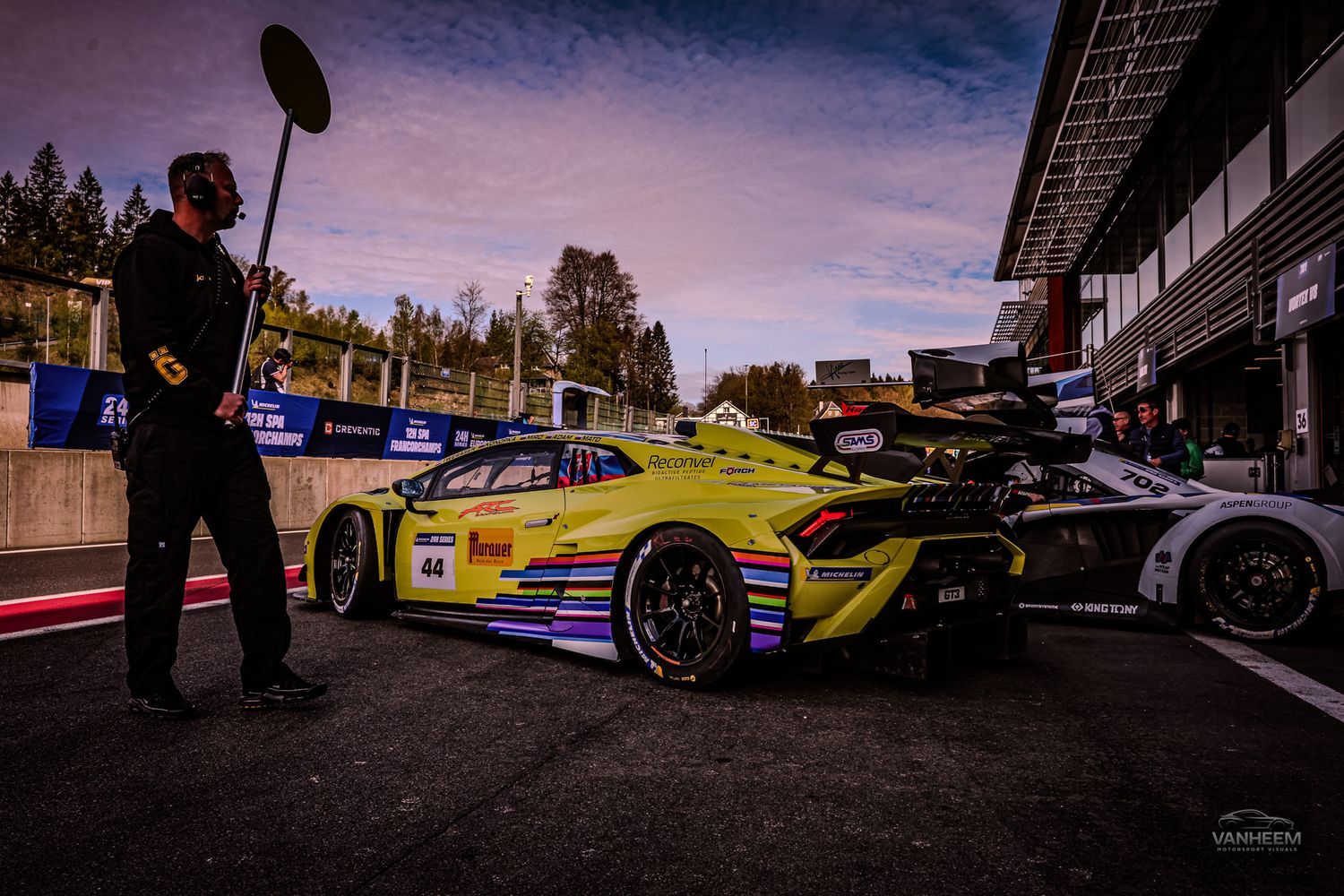 Yellow Lamborghini GT3 race car number 48 in pit lane at motorsport circuit with crew member standing nearby.