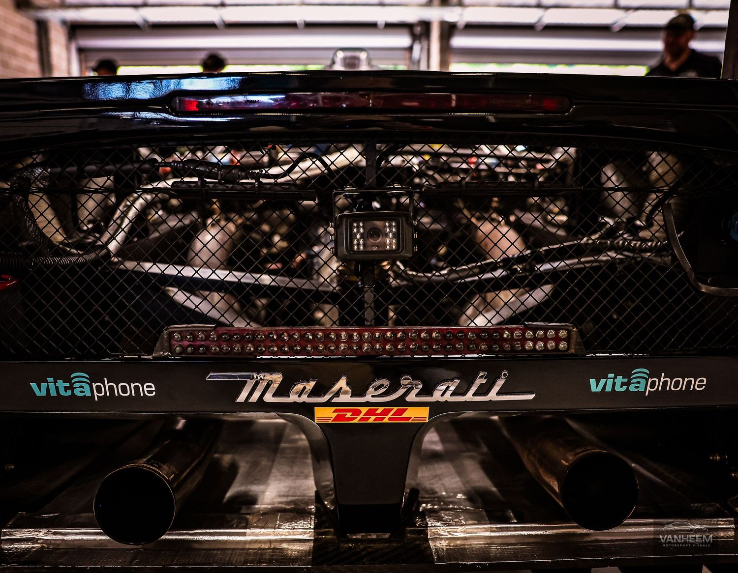 Close-up of a Maserati race car engine bay with Vitaphone Racing branding and dual exhaust pipes.