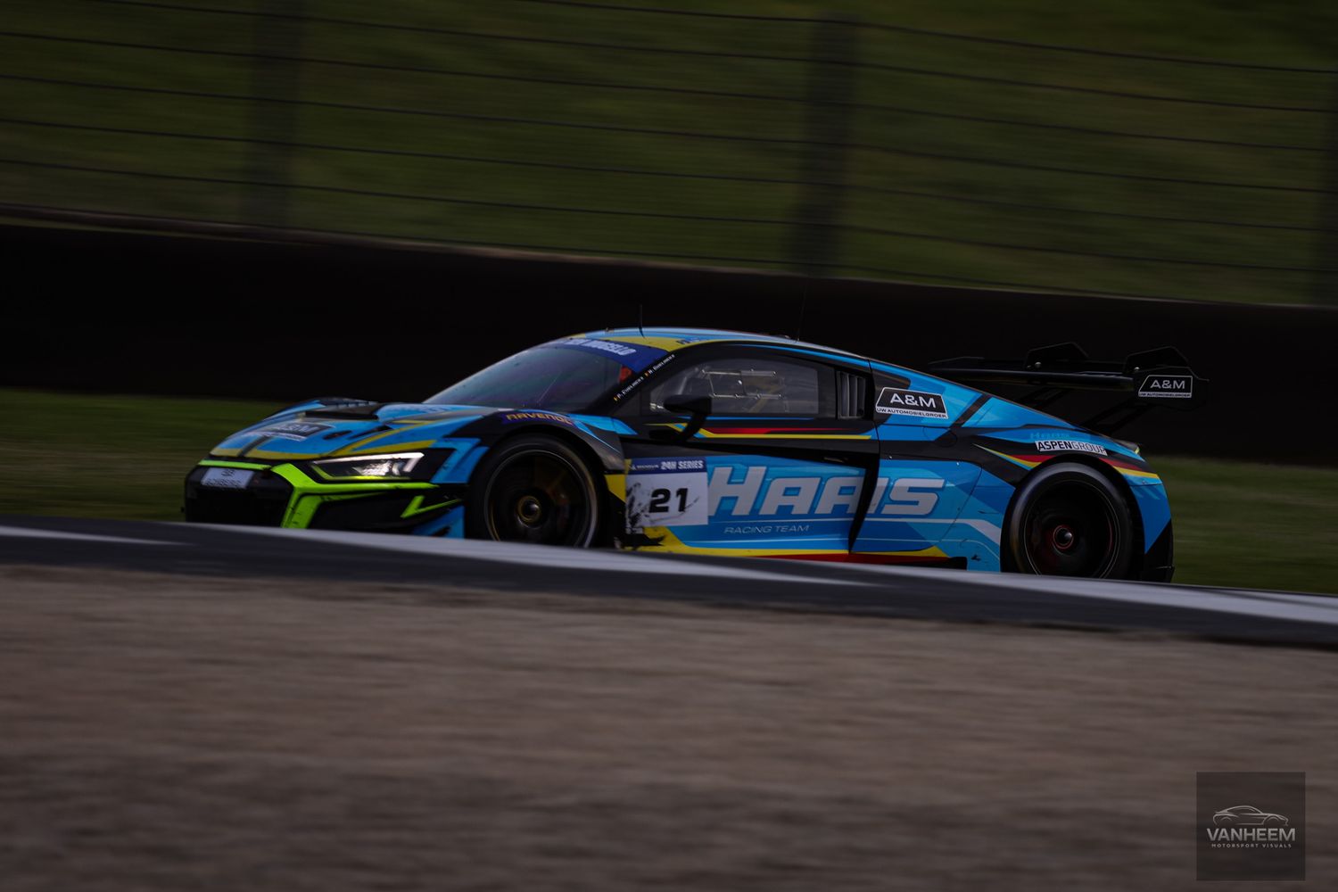 Blue and black race car speeds around a racetrack during a competitive motorsport event.