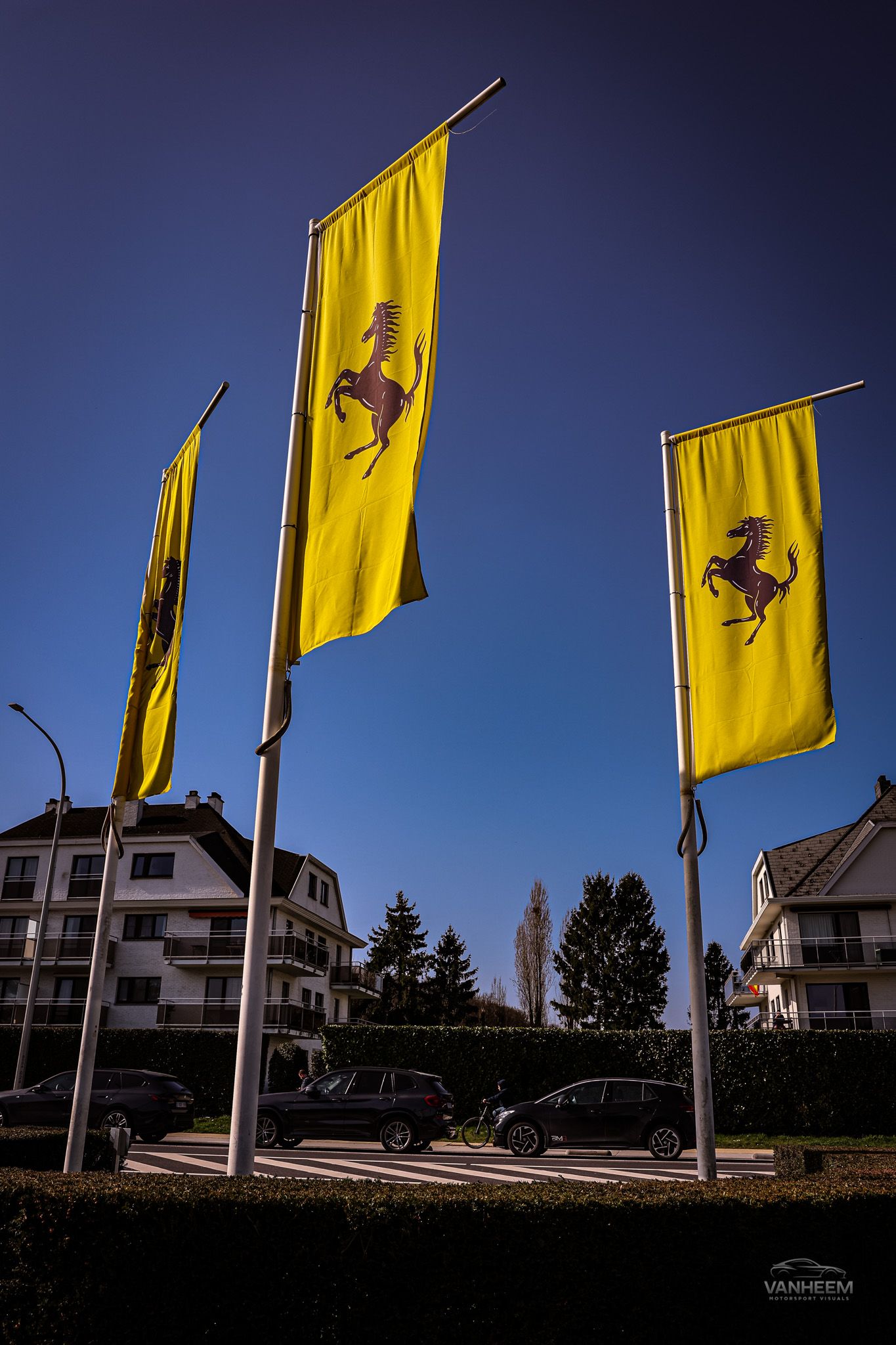 Row of yellow Ferrari flags waving against a blue sky outside a dealership.