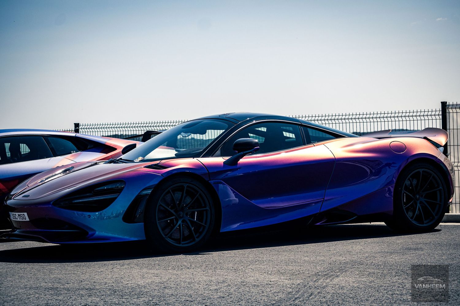 Seven luxury supercars in vibrant colors lined up at a racetrack with dramatic lighting and angles.