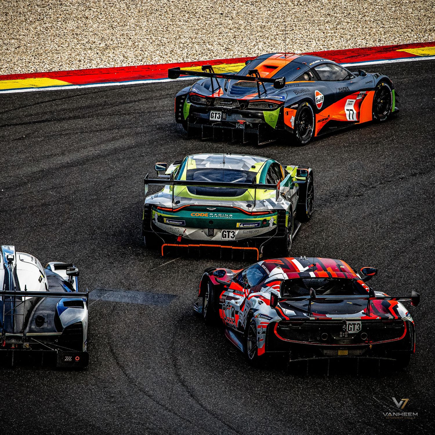Multiple GT racing cars including McLaren and Aston Martin models competing on a circuit track during a motorsport endurance race.
