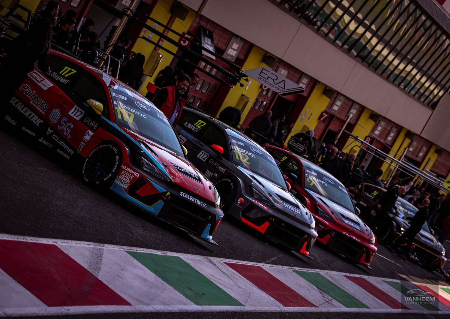 Row of classic Ferrari race cars lined up on a track with red and green striped curbing.