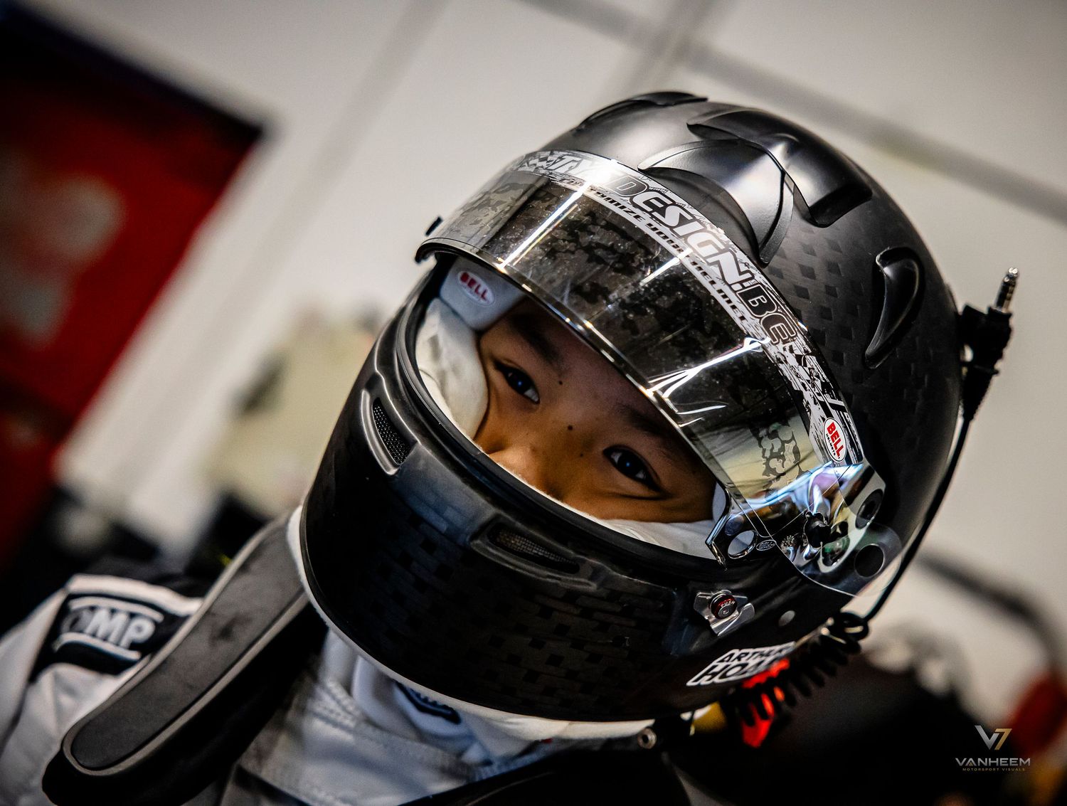 Young karting driver wearing a black carbon fiber racing helmet with visor up, ready to race.