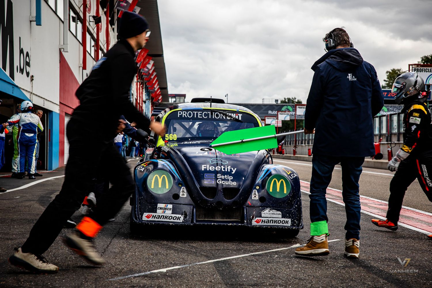 Race car with McDonald's and Protection One livery in pit lane, crew members pushing vehicle at motorsport event.