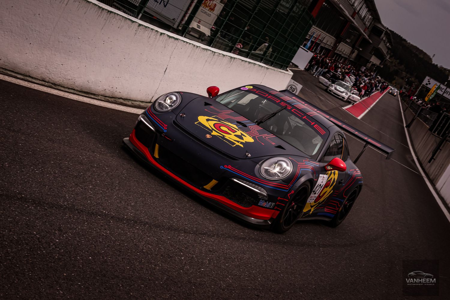 Purple and red livery Porsche 911 GT3 race car on Spa-Francorchamps pit lane.