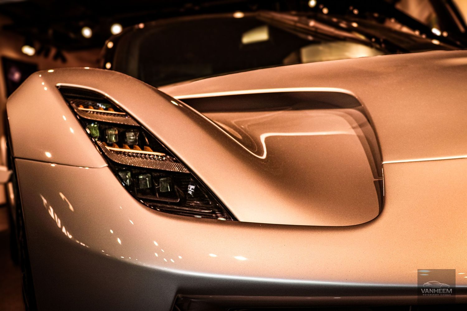 Close-up of a sleek silver supercar headlight and hood detail showcasing luxury automotive design at an auto show.