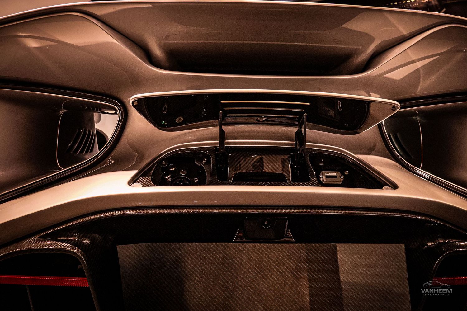 Close-up view of a supercar engine bay with carbon fiber components and rear spoiler under dramatic lighting.