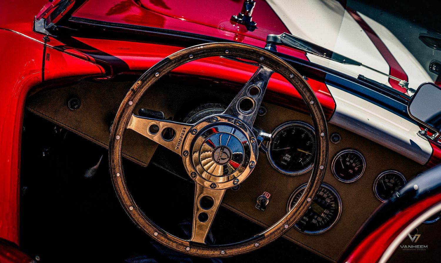 Close-up of a classic red sports car interior featuring a wooden steering wheel and vintage dashboard gauges.