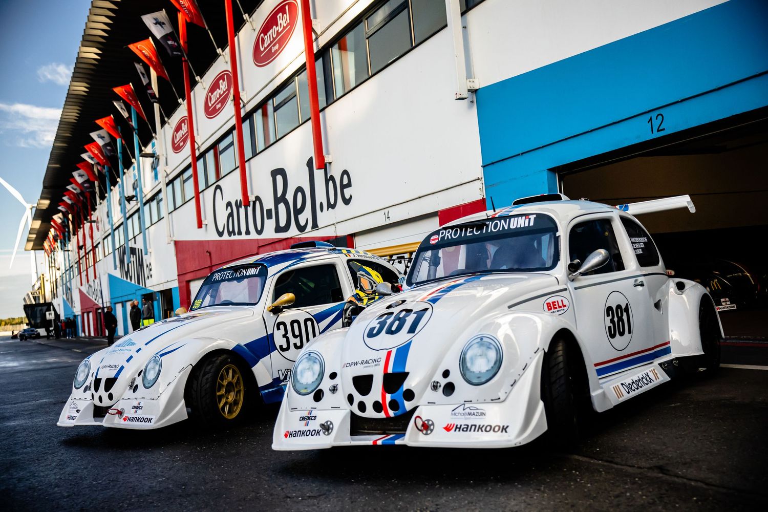 Two Herbie-style VW Beetle race cars numbered 390 and 381 parked at Circuit Zolder pit lane.