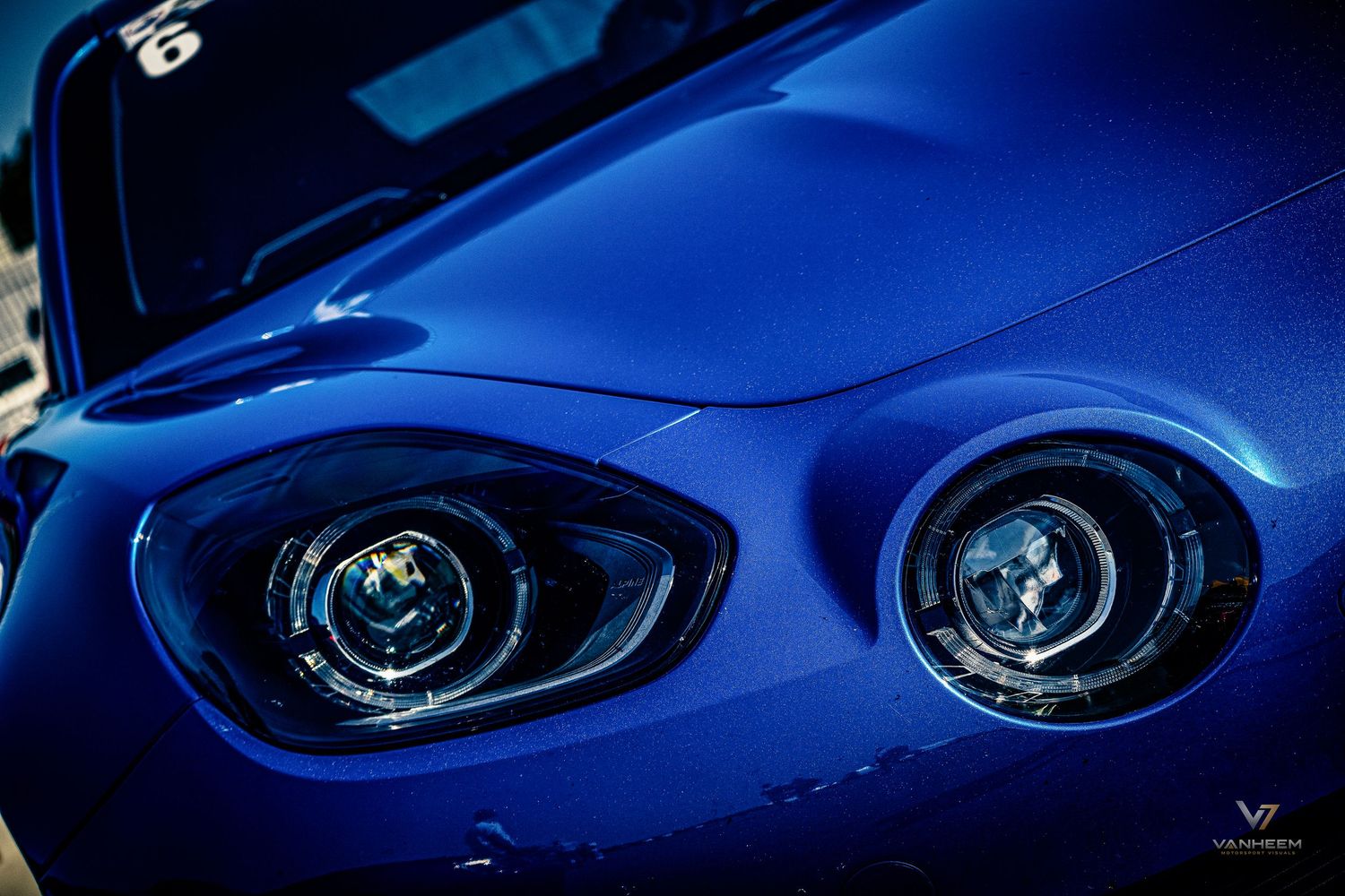 Close-up of a blue sports car's dual headlights with sleek aerodynamic hood design.