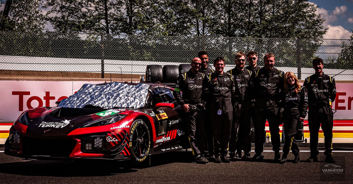 Racing team poses beside a red GT race car at a motorsport circuit with TotalEnergies branding in background.