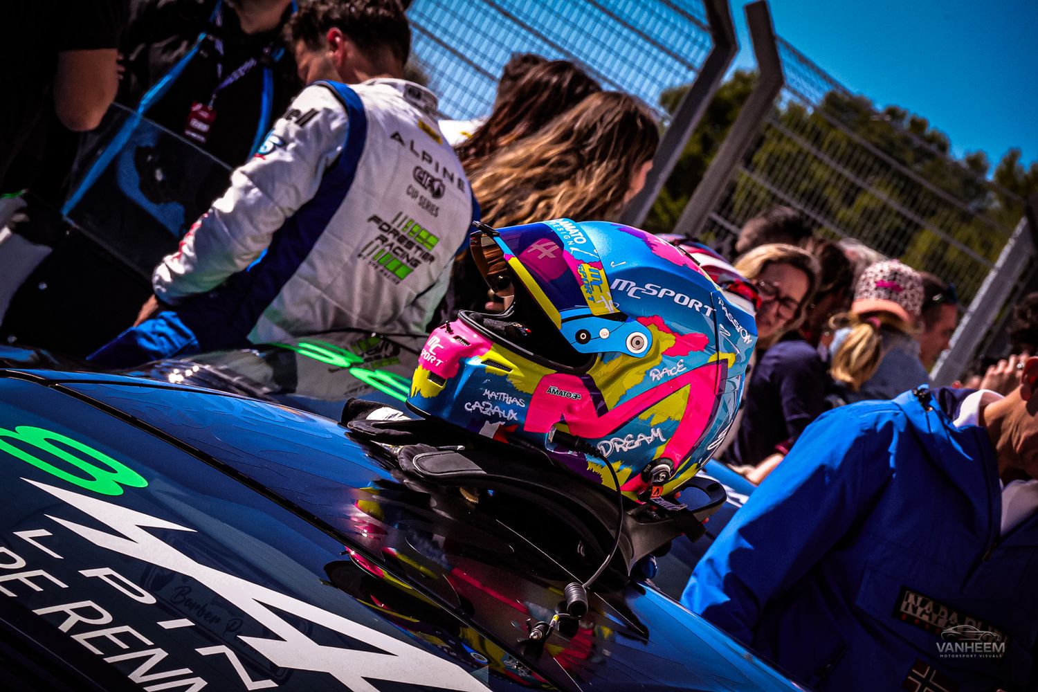 Race cars in vibrant blue and pink liveries competing on a professional racing circuit.