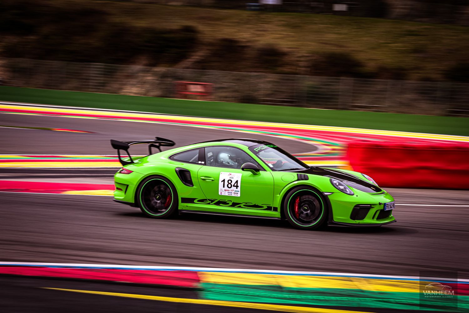 Lime green Porsche 911 GT3 RS number 184 racing on a track at Spa-Francorchamps circuit.