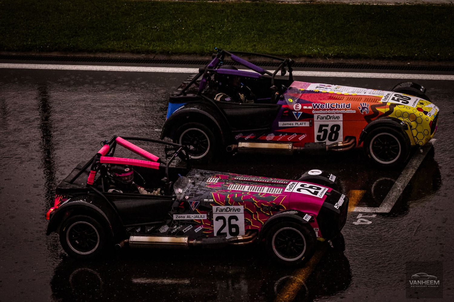 Two colorful race cars numbered 58 and 26 competing on a wet track in rainy conditions.