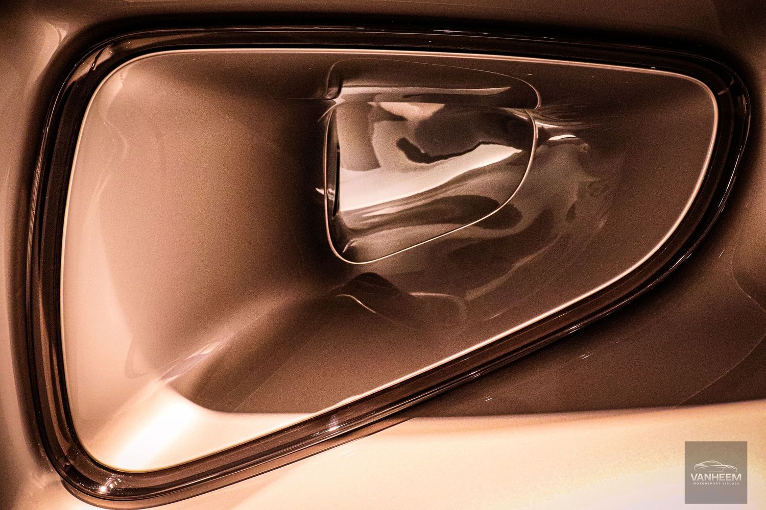 Close-up of a sleek bronze car door handle recess with smooth curved surfaces and glossy finish.