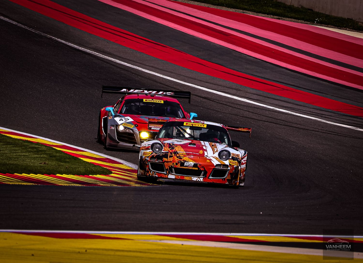 Two Porsche GT3 race cars compete on a dramatic red-curbed circuit during an endurance race.