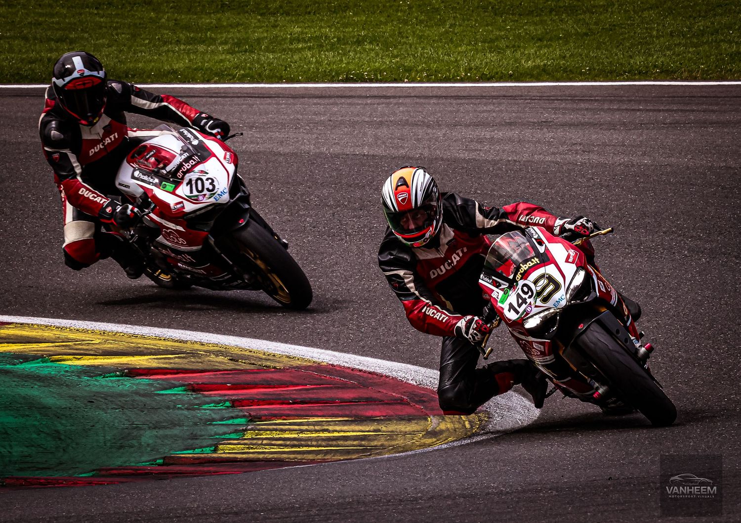 Two motorcycle racers compete on a circuit track, leaning into a curve at high speed during a professional road racing event.