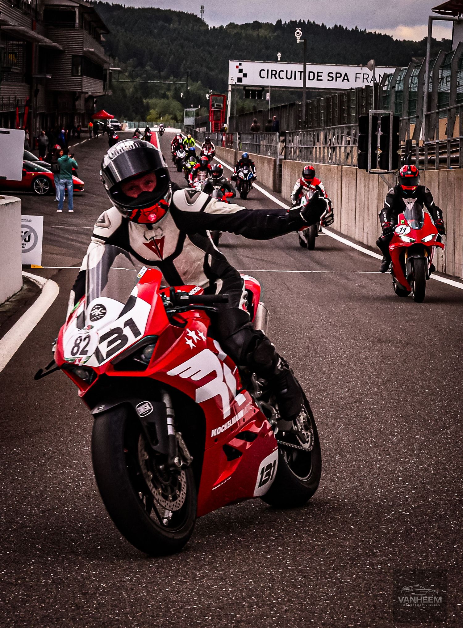 Motorcyclists in racing gear on red bikes at Circuit de Spa-Francorchamps, with rider #82 leading the pack.