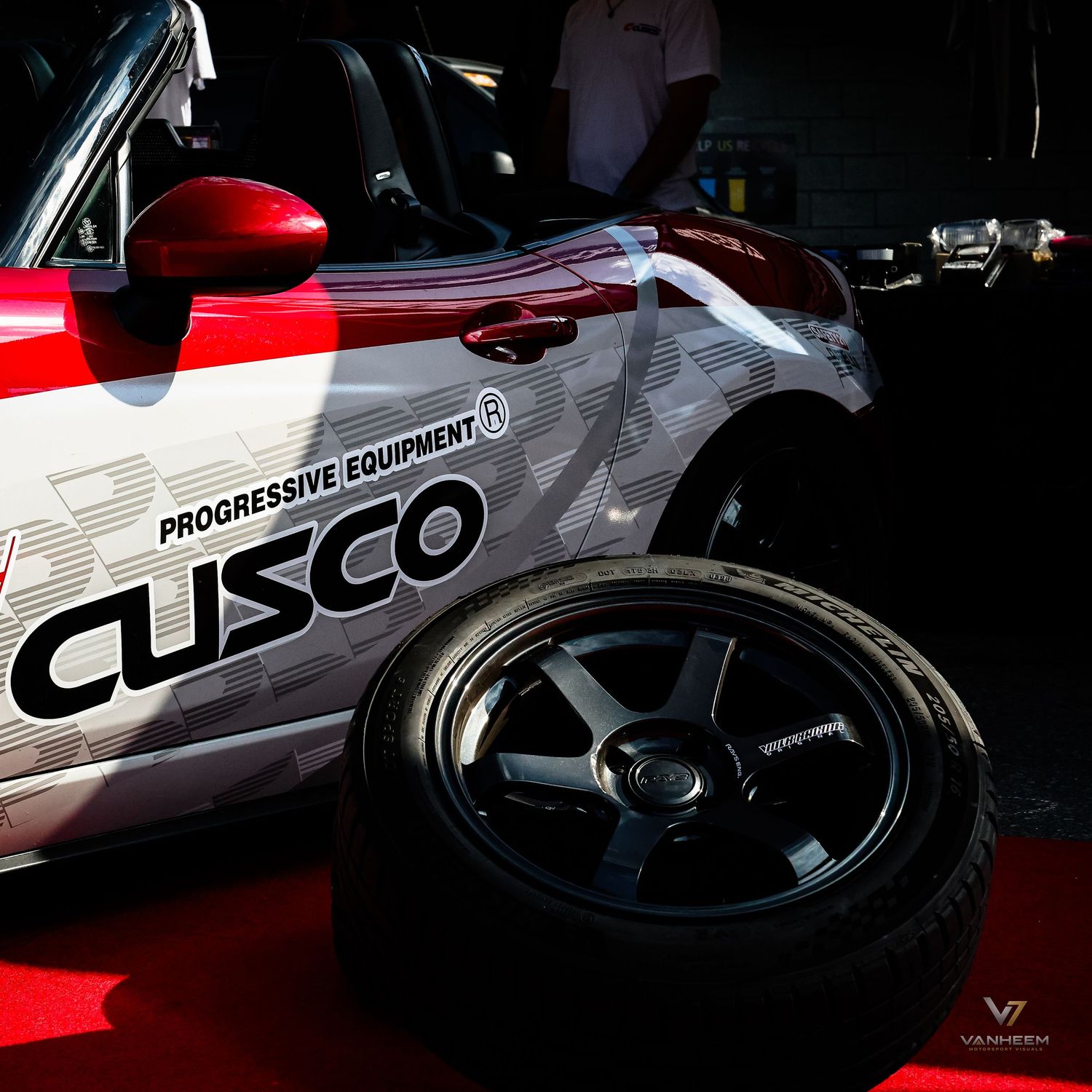 Cusco Progressive Equipment branded race car with black alloy wheel displayed on red carpet at automotive event.