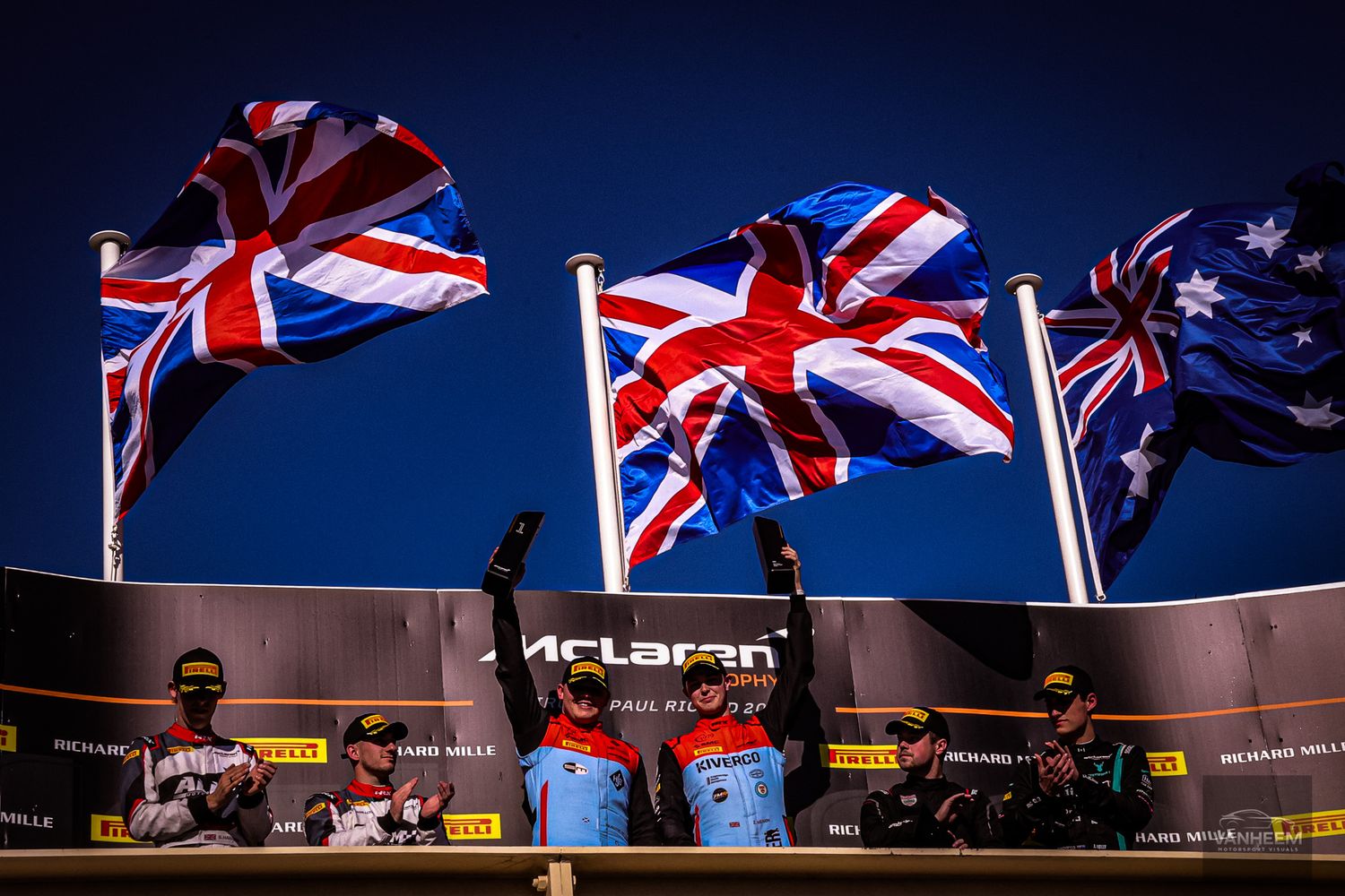 British Union Jack flags wave against a dark blue sky at a McLaren racing event.
