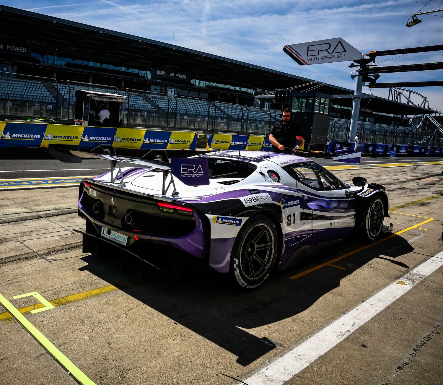 Purple ERA racing car in pit lane at motorsport circuit with Michelin signage visible in background.