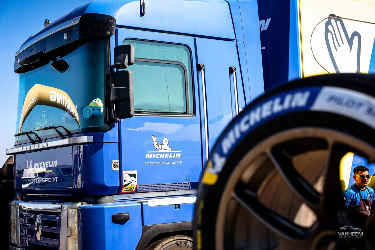 Blue Michelin-sponsored truck with Pilot Sport tire in foreground at motorsport event.