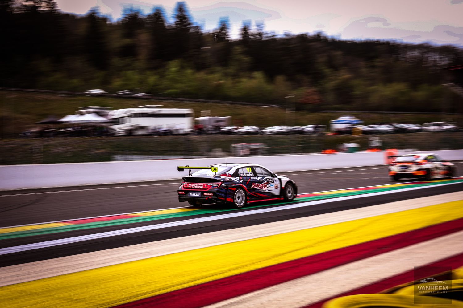 A Porsche race car speeds along the Spa-Francorchamps circuit during a motorsport competition.