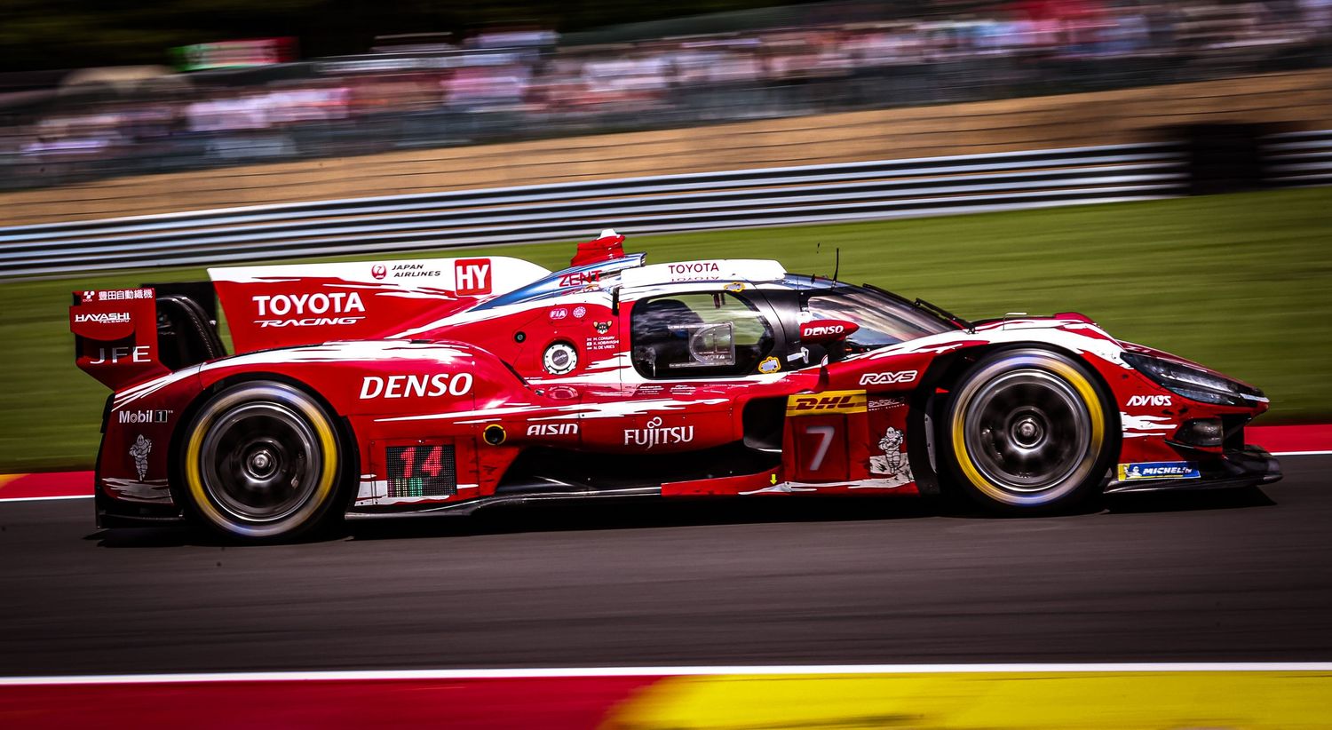 Toyota Denso red racing car speeding on track during endurance race competition.