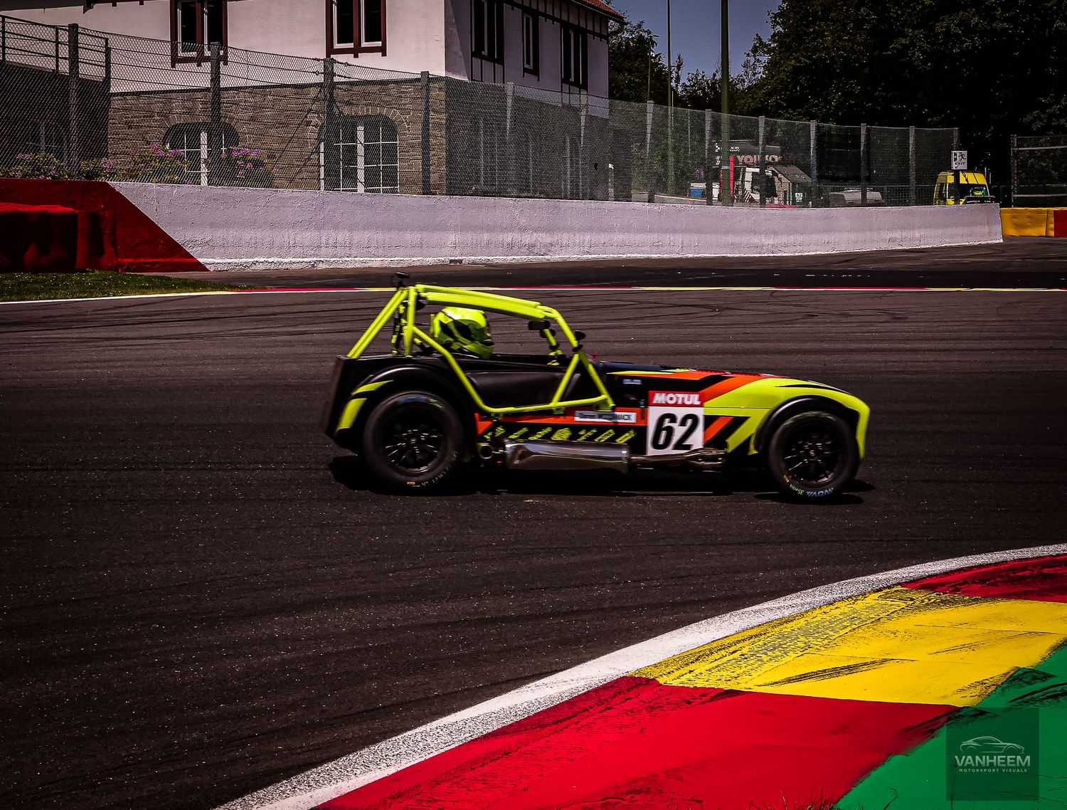 Yellow and black race car number 62 speeding on a circuit track with colorful curbing visible in the foreground.