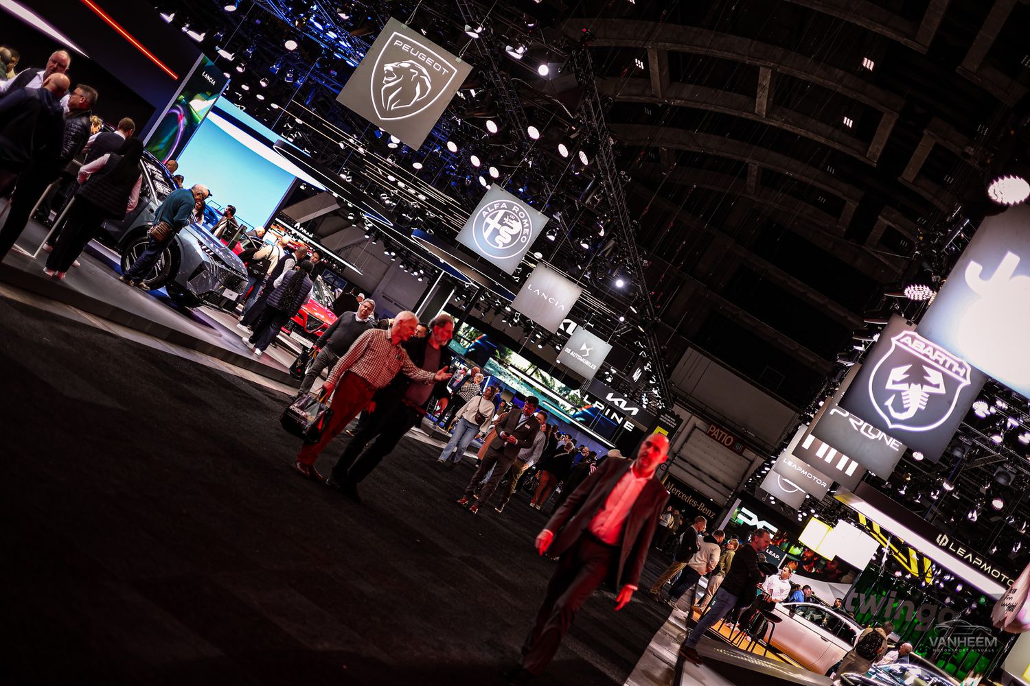 Wide view of busy auto show floor with multiple vehicle displays and exhibition stands.