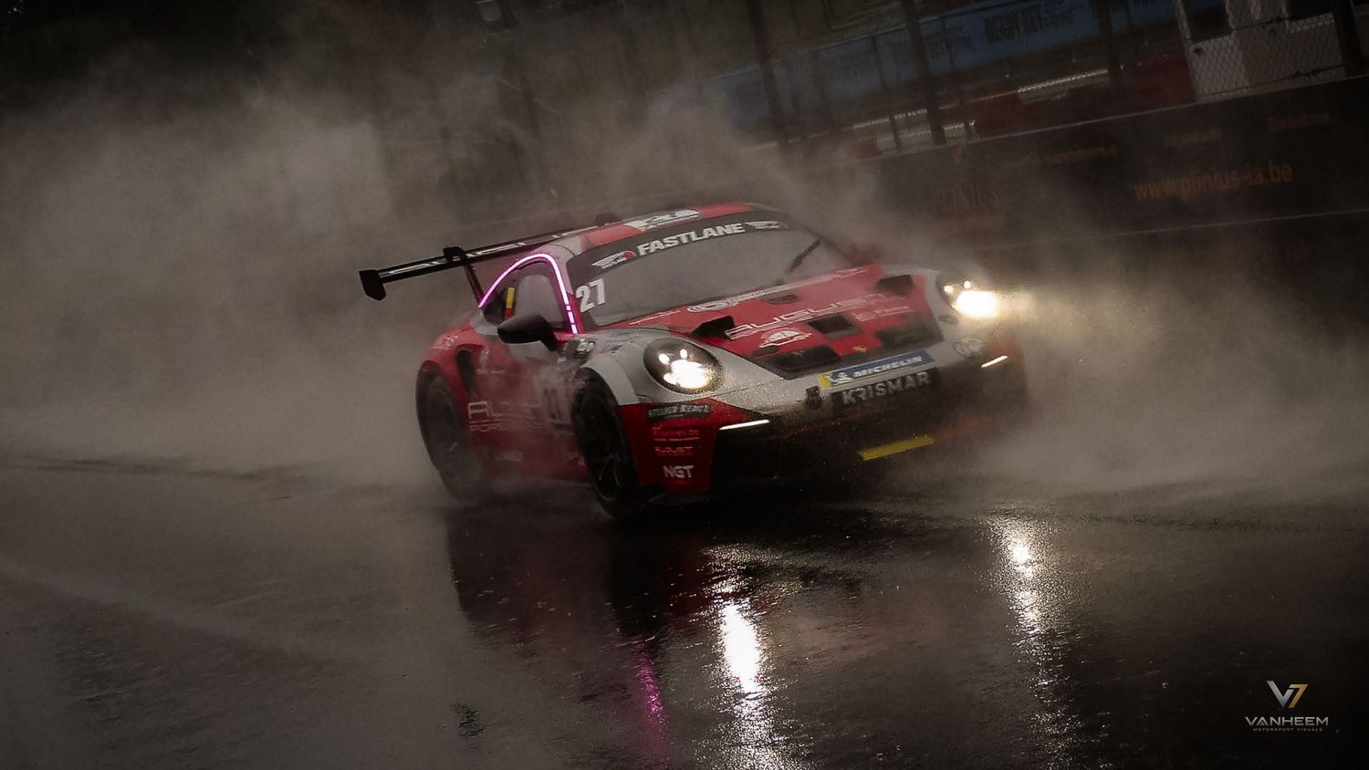 A red racing car speeds through heavy rain on a wet track, spraying water dramatically under moody, dark conditions.