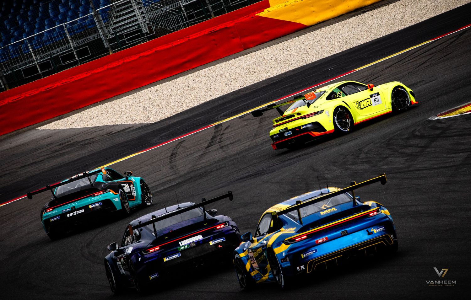 Multiple colorful Porsche GT3 race cars competing on a professional racing circuit during an endurance motorsport event.