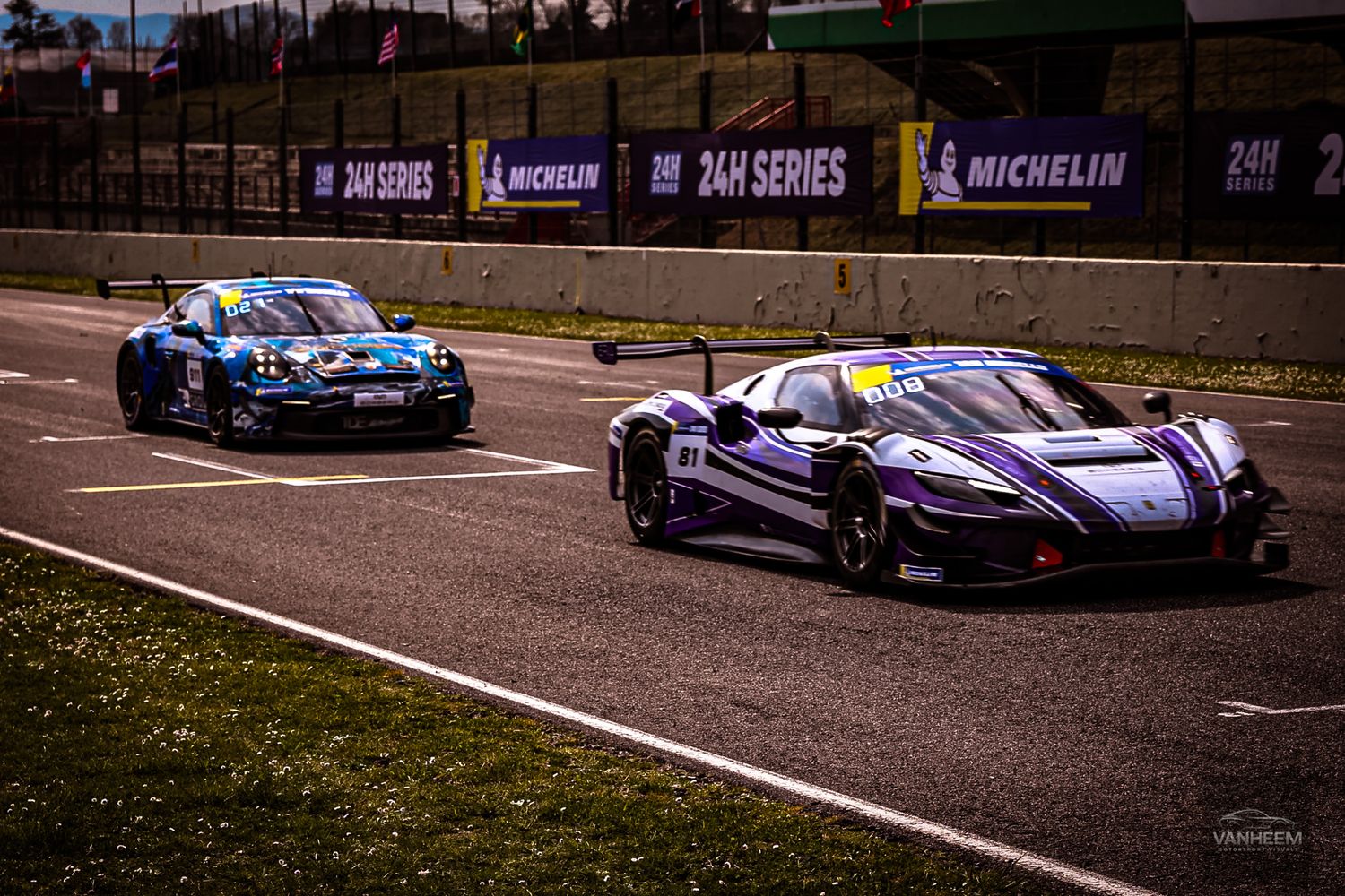 Racing cars navigate through a winding track during a competitive motorsport event at sunset.