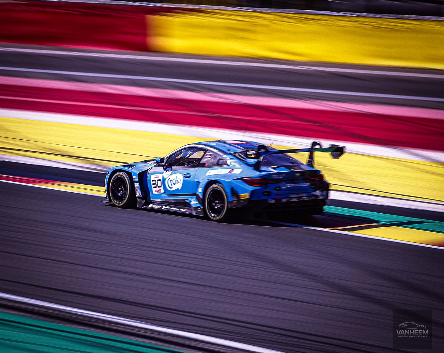 Sports car racing on a colorful track with distinctive red and yellow safety barriers.