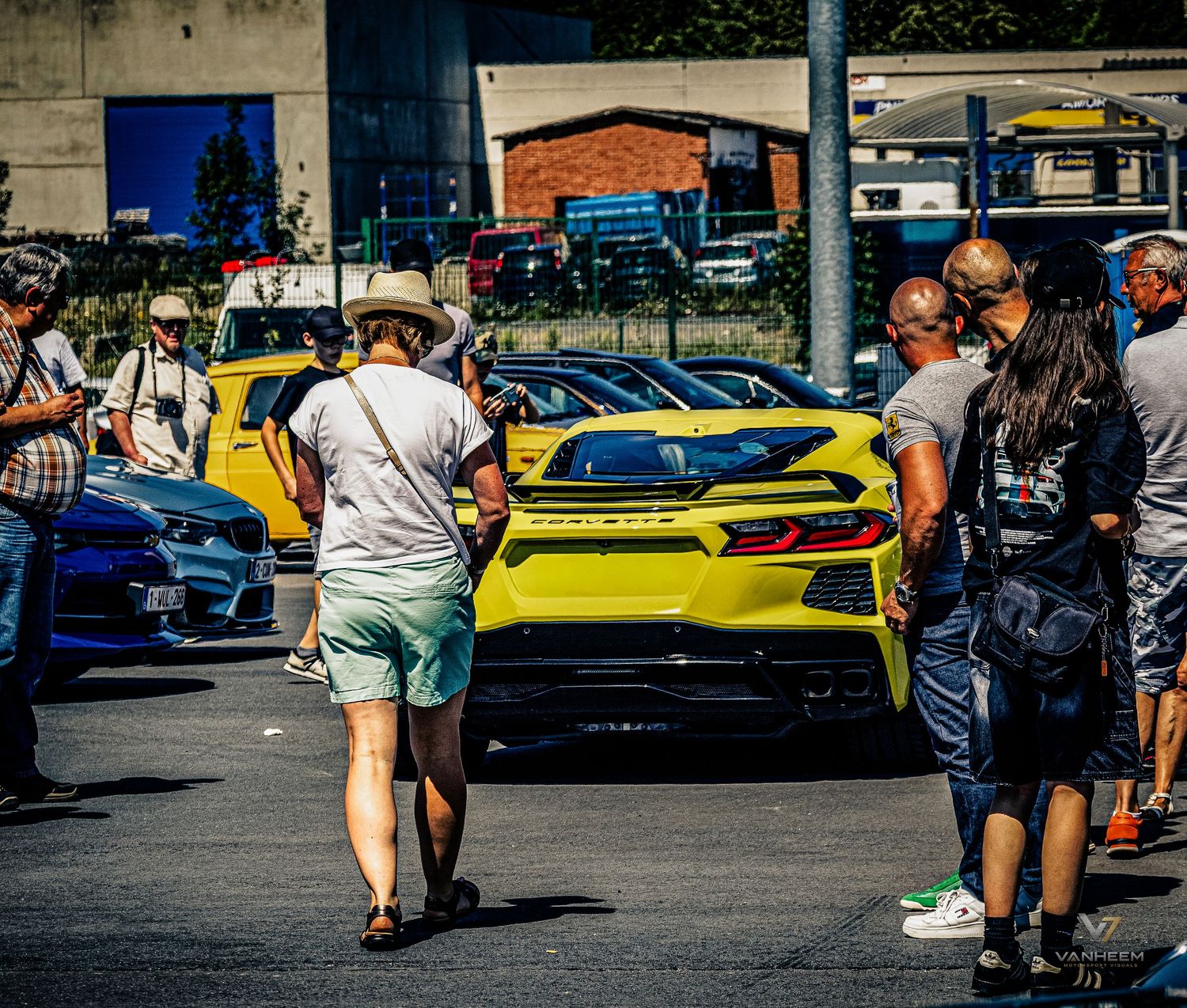People admiring a bright yellow Corvette sports car at an outdoor car show on a sunny day.