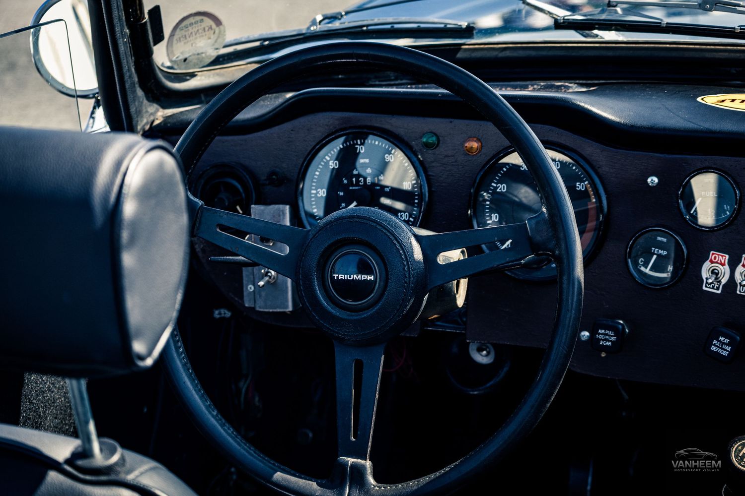Close-up view of vintage car dashboard showing classic gauges, steering wheel and interior details in dark lighting.