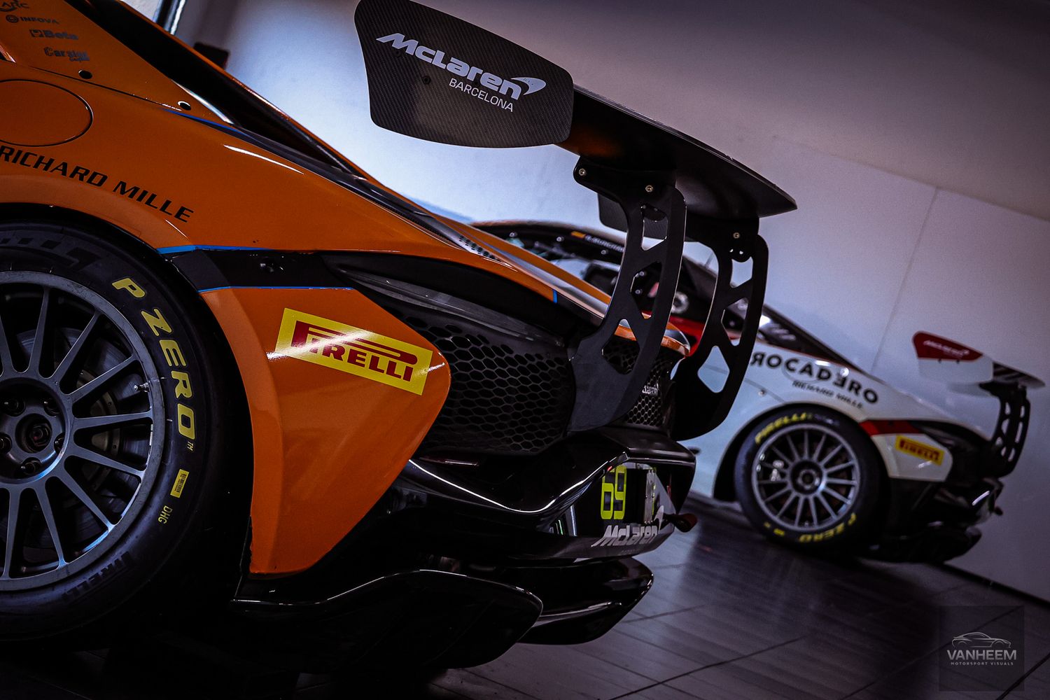 Dramatic low-angle view of McLaren race cars in dimly lit garage.