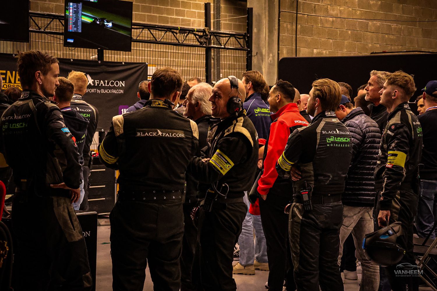 A large crowd of people gathers in a dimly lit indoor venue with brick walls and industrial lighting.