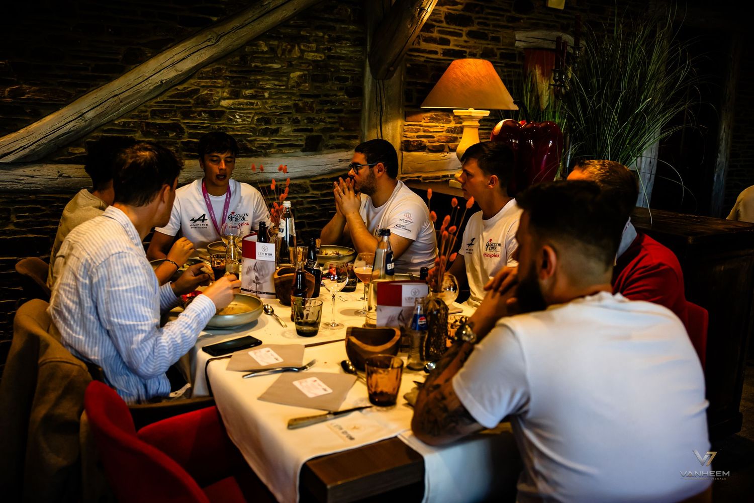 Group of men dining together at a restaurant table with wine bottles and warm ambient lighting.