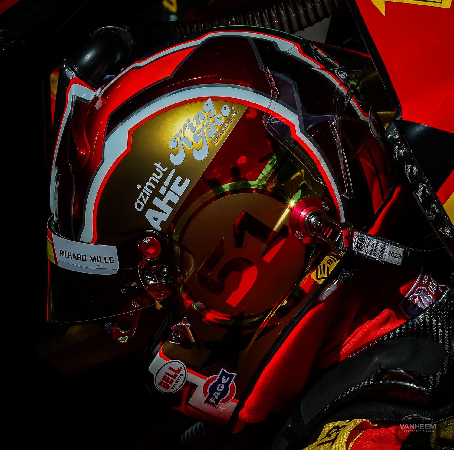 A MotoGP rider wearing a red Ferrari helmet with Richard Mille branding sits in their race car cockpit.